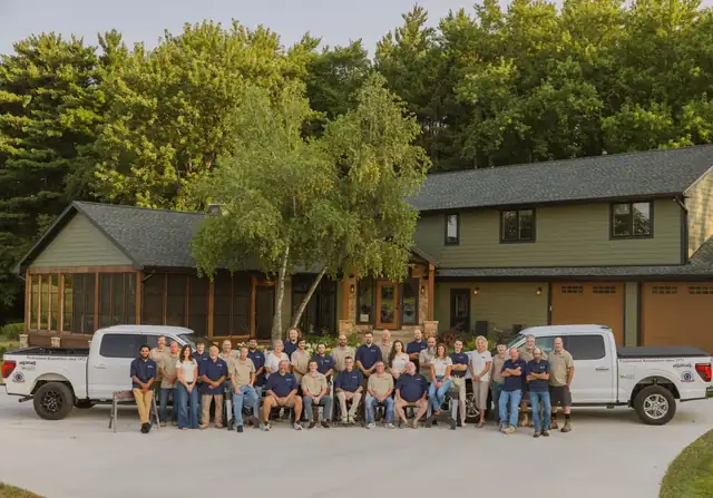 The Stebnitz Builders team gathered in front of a green-sided home with two white company pickup trucks