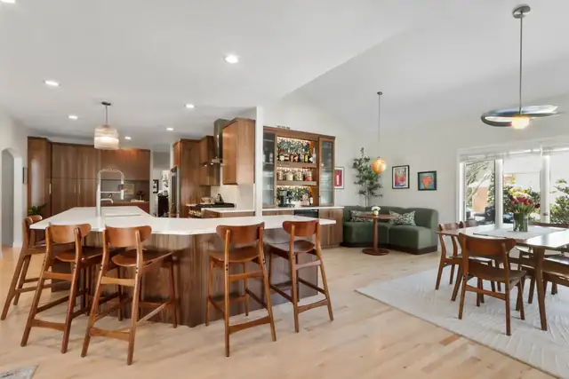 Open kitchen with walnut cabinets, a white quartz island with wood counter stools and a dining area by the windows
