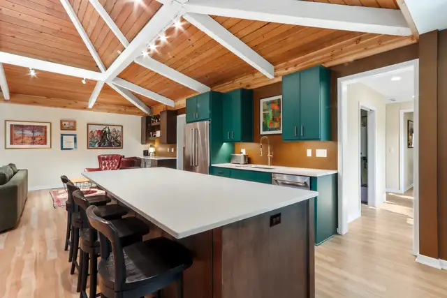 Whole home remodel with green kitchen cabinets, wood plank vaulted ceiling with white beams and a large quartz island