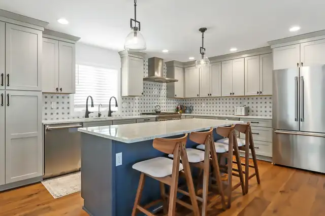 Kitchen with gray shaker cabinets, navy island with wood stools, patterned tile backsplash and stainless appliances