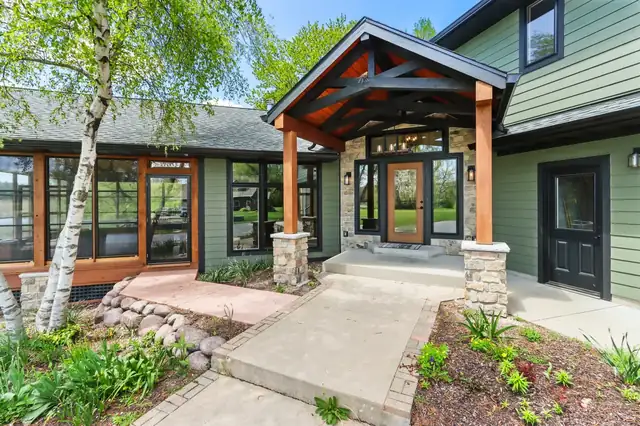 Remodeled home entry with timber-frame gable porch, stone columns, wood front door and green siding