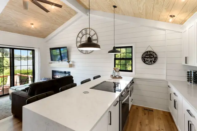 Lake cottage kitchen with white shiplap walls, waterfall quartz island, black pendant lights and patio doors to the water