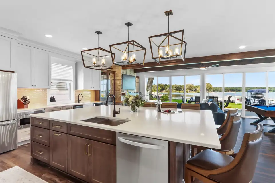 Kitchen remodeling Elkhorn area: lake-view kitchen with long white quartz island, walnut base cabinets, black geometric pendants and wall of windows