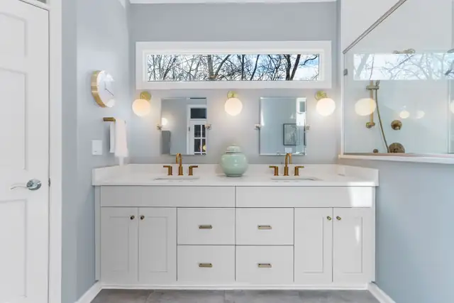Bathroom remodel with white double vanity, brass faucets and sconces, transom window and frameless glass shower