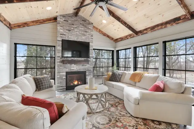 Sunroom with a stacked stone fireplace, knotty pine vaulted ceiling, black-framed windows and white sofas