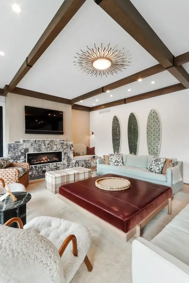 Living room with dark wood ceiling beams, a sunburst light, a linear fireplace and a red leather ottoman